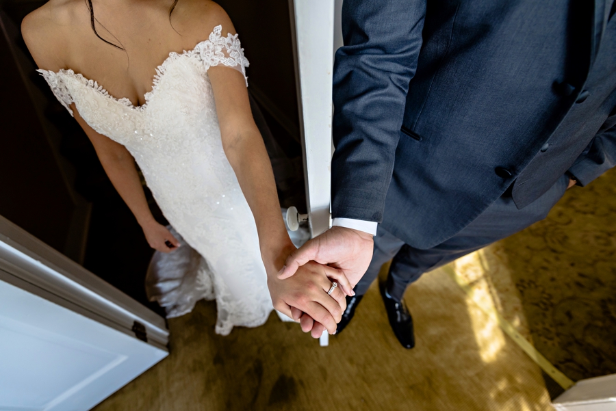 A couple hold hands before the wedding ceremony while separated by a door.